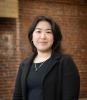 Picture of an Asian woman in black standing in front of a red brick wall