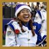 a photo of Idriana Jan Abinales. She is wearing a UW marching band uniform and a purple hat. She has two brown braids and glasses.