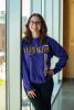 Moira Kelley, a UW student employee, stands inside by large glass windows with a purple UW sweatshirt on.