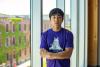 Regan Lai, a student employee, stands in front of large glass windows, wearing a purple UW t shirt.