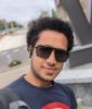 photo of Ram Krishnan. He has short curly black hair and he is wearing black sunglasses and a dark blue t-shirt. He is standing in front of the W statue on campus. 